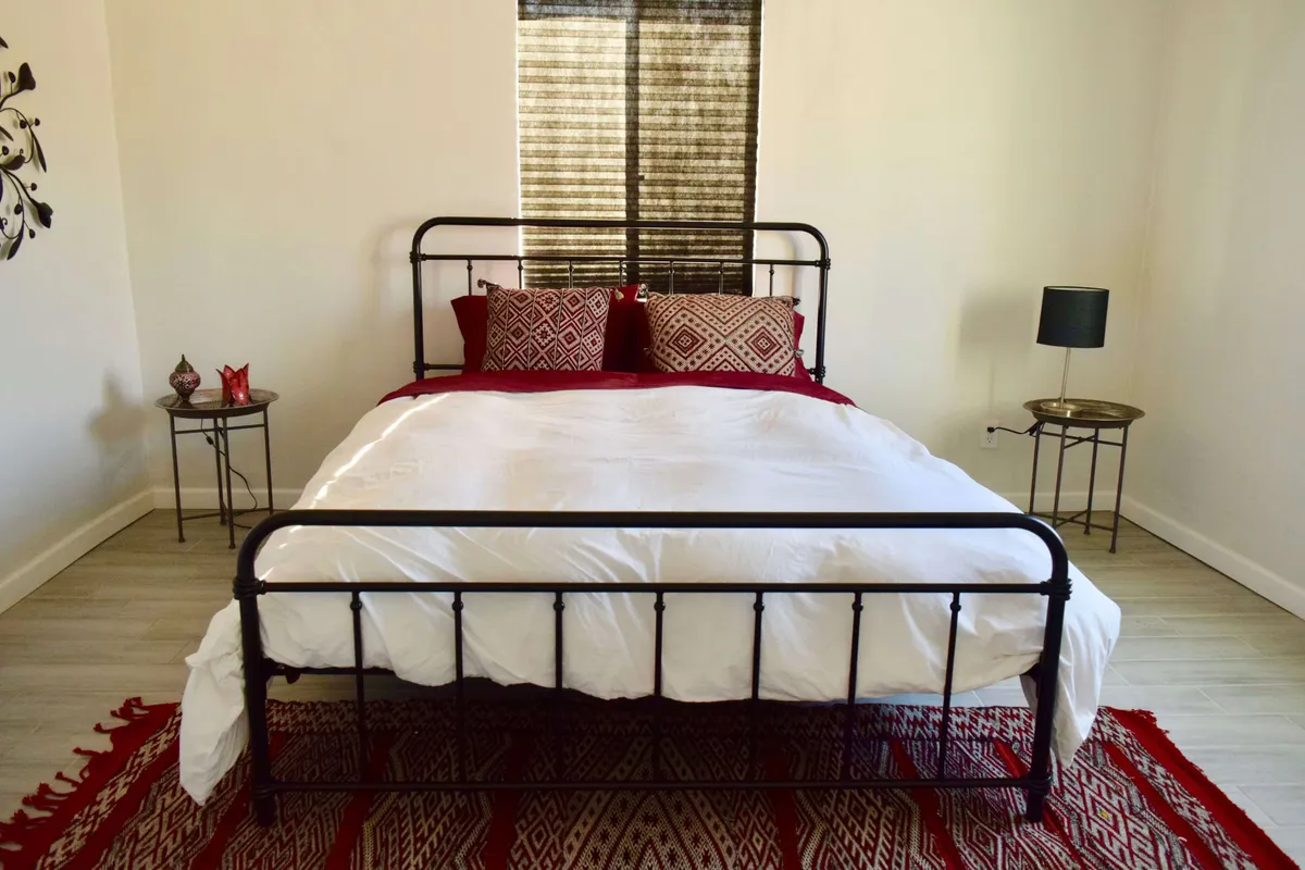 Another inviting bedroom with a comfortable bed dressed in decorative pillows, a soft rug underfoot, and matching side tables. The room is brightened by natural light, enhancing the tranquil and rejuvenating atmosphere. The visible tile flooring ties back to the section's details on materials and comfort.
