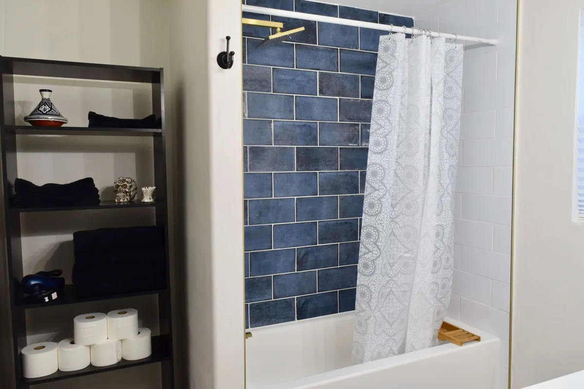 This interior image shows a bathroom with a blue tiled wall, a shower curtain, and a shelf stocked with towels. The overall ambiance is soothing, and the space is organized and modern.